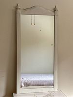 Full view of the tall rectangular mirror hung upright on a wall, showing wooden frame and mirror surface.