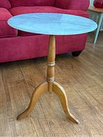 Full view of round side table showing white marble top and wooden base with three curved legs on hardwood floor.