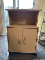 Front view of wooden microwave cart on wheels with two closed cabinet doors and open top shelf.