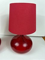 Single red glass table lamp with red fabric shade, rounded base on white background