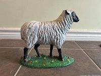 Front view of cast iron sheep or lamb painted doorstop with detailed painting and flower-accented green base.