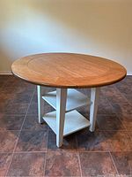 Round wooden table with foldable sides and painted white base with two shelves.