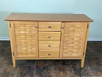 Front view of the wooden sideboard showing woven veneer door panels, four center drawers, and metal knobs.