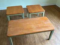 Image showing two square end tables and a rectangular coffee table with wooden tops and green legs placed on wooden floor under natural light.