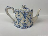 Side view of the ceramic tea pot showing detailed blue vine floral exterior with curved spout and handle.
