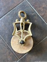 Front view of vintage pulley shows wooden wheel and decorative cast iron frame with top eyelet.
