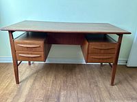 Full front view of teak desk showing top, drawer blocks, and tapered legs