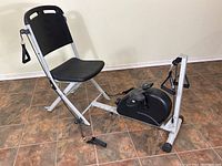 Full view of the VQ Action Care foldable resistance exercise chair showing the padded seat, backrest, pedal resistance unit, and base frame on tiled floor.