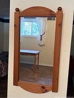 Full view of wood framed rectangular mirror mounted on wall, showing natural wood color and arched top edge.
