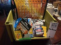 Yellow container holding assorted batteries including unopened packs of Duracell AA batteries, Energizer AA batteries, and other batteries loose or in packaging.