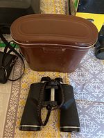 Four binoculars shown including one Bushnell model with brown case on patterned surface.