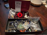 Overview photo of the entire lot showing carved stone necklace, cufflinks, pins, badges, and buttons in an open box with seller label