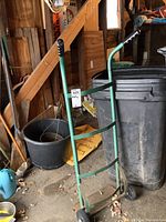 The full dolly in a garage environment showing handles with black grips, green metal frame, and some surrounding items.