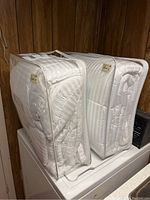 Two white down-alternative duvets packaged in clear plastic zippered bags, placed on top of a washing machine in a wood-paneled room.