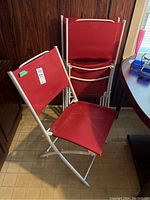 Three red fabric folding patio chairs with white metal frames, some stacked, showing front and side views.