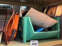 Green bin containing assorted workshop accessories such as circular saw blades and wire brushes