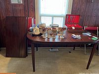 Full view of the dining table with two wooden leaves positioned to the side. Table top has various ceramic and metal items not included.