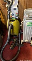 Overall view of yellow canister vacuum with hose, wand and adjacent heater