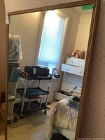 Full view of the large wall mirror leaning against a wall, showing the reflective surface and decorative frame detail.