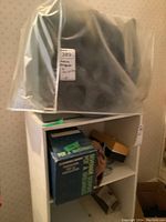 Overall view of the projector covered in plastic on a shelf, with boxes below containing accessories