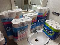 Multiple unopened packages of Cashmere toilet paper and a package of Sponge Towels paper towels displayed near a sink.