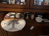 Wide shot showing place mats, tape rolls, ceramic items and cups on wooden shelf
