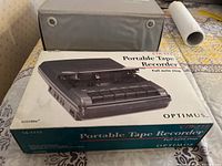 Front view of the Optimus portable tape recorder in original box with protective case behind