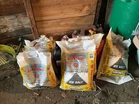 Bags of yellow and white siflo SafeStep ice salt and two black plastic jerry cans in a wooden garage.