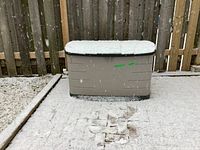 Rubbermaid resin deck box placed outdoors on a deck under snowfall, closed lid with snow accumulation