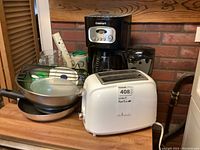 Full lot view showing all items together on a wooden counter including toaster, coffee maker, can opener, frying pans stacked, and mixing bowl.