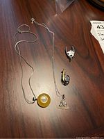 Photo showing two necklaces and two pins on wooden surface, details of each item visible.