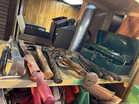 Shelf stocked with various hand tools including hammers, crowbars, and a green fish tackle box.