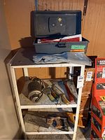 Wide view of shelf with toolbox, work gloves on top, electric heater and hammer on middle shelf, and hand saw on bottom shelf