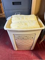 Photo of white plastic laundry hamper filled with folded yellow towels.