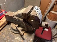Metal bench vise positioned on a workbench, showing its general wear, screw mechanism, and handle.