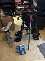 Walker with padded seat labeled Nexus, cane, medical boot, patellar sleeve in box, and medical book placed on floor.