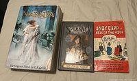 Photo of three assorted books on a light-colored surface including The Chronicles of Narnia box set, The Spiderwick Chronicles The Field Guide, and Andy Capp Man of the Hour comic book.