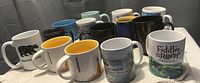 Photo of nine assorted coffee mugs showing various designs and colors including black, white, and blue mugs with yellow and black interiors