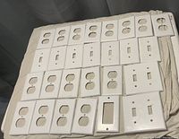 Top-down view of assorted white plastic light switch and receptacle covers laid out flat on fabric.