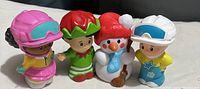 Four Little People toys including girl in pink helmet, elf, snowman, and boy in white helmet.