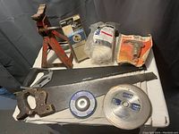 Full view of lot showing hand saw, red jack stand, two branded cutting discs, and three boxed/hanging hardware items including a white nylon rope, metal valve and another item.