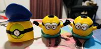 Three plastic Minion toys; one with a blue police hat, two with small black tufts of hair.