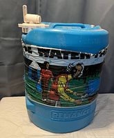 Photo of blue Reliance water cooler with wooden tap and paper label wrapped around body.