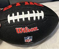 Close-up of Wilson logo and NFL logo on black textured football surface with white laces visible.