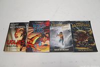 Four paperback graphic novels arranged side by side showing front covers: Uglies: Shay's Story, Wings of Fire #1 The Dragonet Prophecy, Percy Jackson The Lightning Thief, Percy Jackson The Sea of Monsters