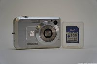 Front view of Casio Exilim EX-Z750 camera with 7.2 Megapixels marking shown next to 1GB SD card in plastic case