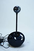 Full view of the Logitech N231 conference camera showing black base with control buttons, vertical stand, and spherical camera head.