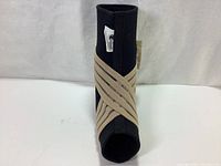 Angled front view of black neoprene ankle support showing beige elastic straps wrapped criss-cross over the ankle support sleeve.