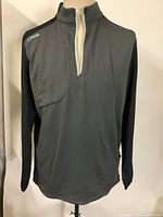 Front view of the black Ping Farrell 1/4 zip golf shirt on a mannequin, showing the standing collar and textured panel on the chest with the Ping logo.