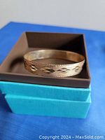Front view of gold bangle resting on two-tone box showing scalloped edge and Navajo motif pattern